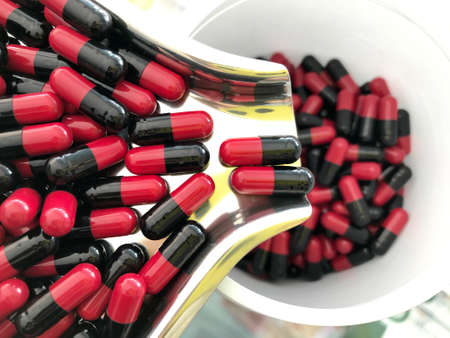 Red and black capsules in tray being poured into the bottleの素材