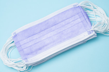 Top view flat lay of a stack of purple medical masks on blue background. Ideal for healthcare,...