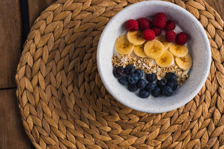 A bowl of fruits, with banana, raspberry and blueberry with oats and yogurt in a wooden backgroundの写真素材