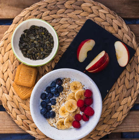 A bowl of fruits, with banana, raspberry and blueberry with oats and yogurt in a wooden backgroundの写真素材