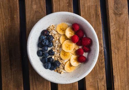 A bowl of fruits, with banana, raspberry and blueberry with oats and yogurt in a wooden backgroundの写真素材