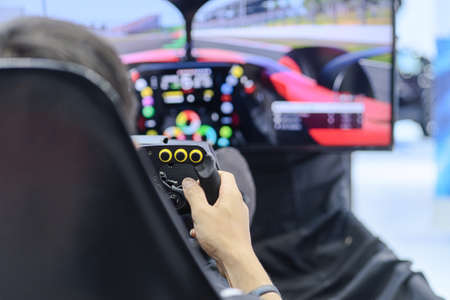Close-up from back view and selective focus right hands of young man gamer who enjoying with racing game via gaming wheel controller on gaming monitor blurred background, entertain on leisure, e-sportの写真素材
