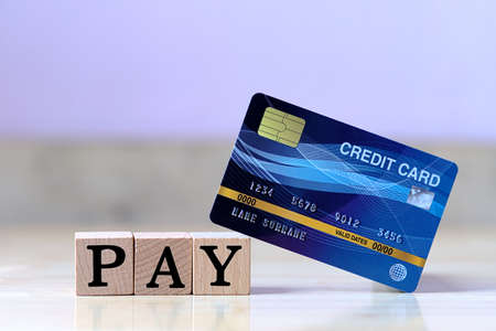 Mock up blue credit card and wood cube letter put on wooden table with spending via credit card Instead of cash conceptの写真素材