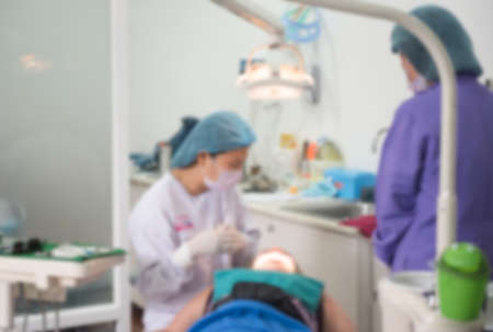 Blurred abstract background of dentistry care unit room interior in dental hospital clinic with dentist and assistants working on patient's tooth care using equipment, instrument on dental chairの写真素材