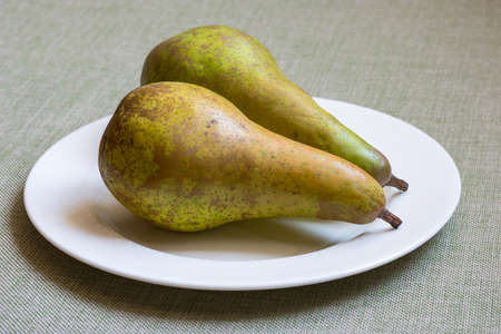 Two green fresh organic pears on white plateの写真素材