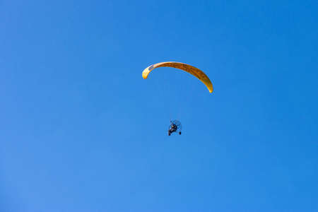 Motoparagliding - flying motorized manned yellow parachute against clear blue skyの写真素材