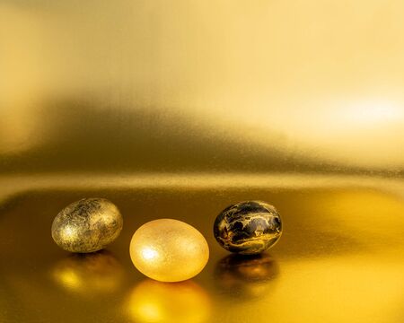 Easter eggs painted in gold and black on a glittering background for the holiday of bright easterの写真素材