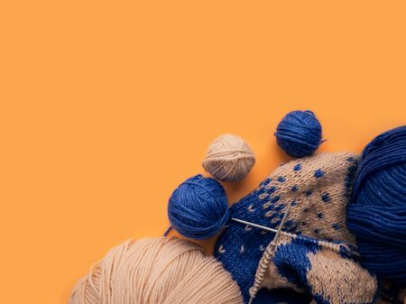 Knitting on needles. Top view of blue and beige yarn balls on an orange background. Hobby.