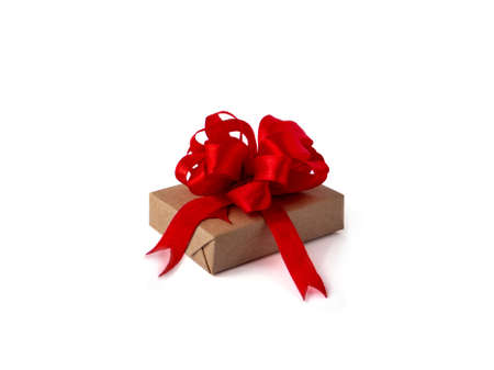 A gift box wrapped in brown craft paper, with a red ribbon and bow on a white, isolated background. concept celebrationの写真素材