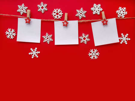 Christmas red background with white snowflakes. Three sheets of paper with space for text on a rope. Topview, copy spaceの写真素材