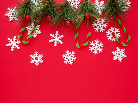 Christmas background with white snowflakes, spruce branch, caramel on red backdrop. Winter holiday...
