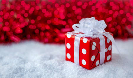 Gift for New year, Christmas, birthday White polka dot box with big bow on red background with bokeh.の写真素材