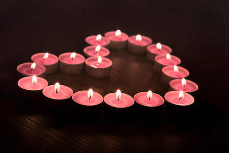 Pink candles are arranged in the shape of a heart on a dark backgroundの写真素材