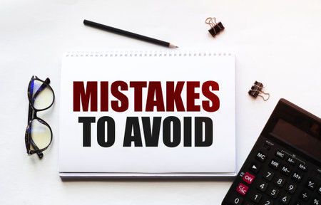 Business concept. Notebook with text Mistakes To Avoid sheet of white paper for notes, calculator, glasses, pencil, pen, in the white backgroundの写真素材