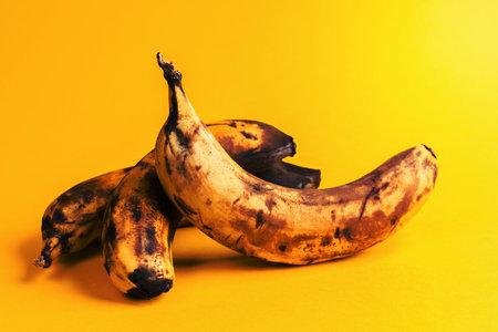 Close-up three overripe blackened ugly bananas on bright yellow background.の写真素材