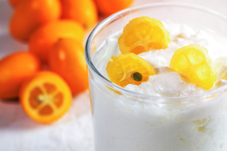 Close-up part of glass cup with homemade yogurt with slices of exotic citrus fruit kumquat on whole fruits background.の写真素材