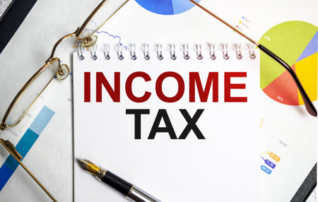 Income Tax text on paper sheet with glasses on chartの写真素材