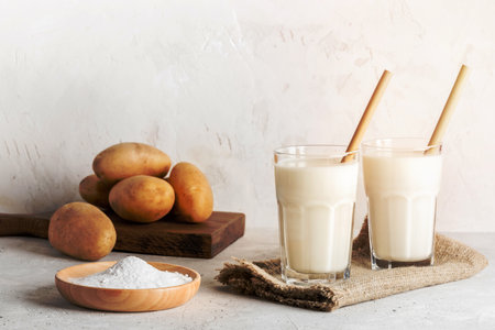 Two glasses of vegan potato milk with bamboo drinking straws, potato tubers and potato powder on neutral backdrop. Powdered vegetable non dairy milk replacer. Selective focus. Horizontal orientation.の写真素材