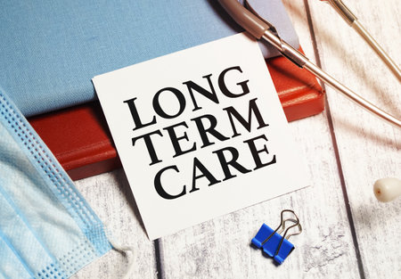 On a light wooden table there is a stethoscope, a pen and a sheet of paper with the text LONG TERM CARE.の写真素材