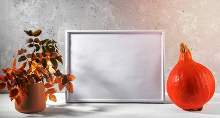 Fall composition with orange pumpkin, empty white frame and color leaves on light background. Thanksgiving day or Halloween mock up. Copy space for text. Banner. Horizontal orientation.の写真素材