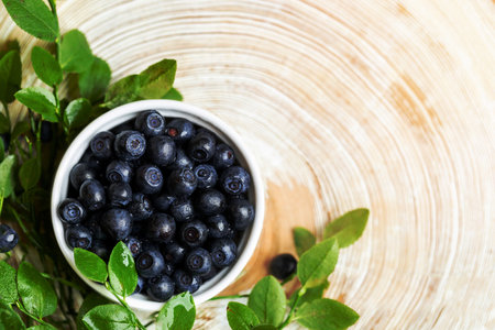 Washed forest blueberries in white bowl and green leaves on wooden saw cut with annual rings. Superfood. Natural healthy food. View from above. Mock up. Copy space for text. Horizontal orientation.の写真素材