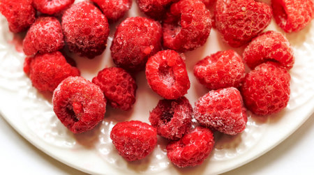 Frozen raspberry on white plate close up. Frozen berries retain all vitamins. Freezing berries are healthy preparations for winter to have vitamins for eating. View from above. Horizontal orientation.の写真素材