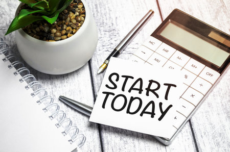 Text start today on paper card and calculator on wooden backgroundの写真素材