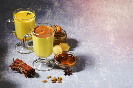 Organic ayurvedic turmeric milk for immunity. Two glasses for mulled wine with golden milk with ingredients on light grey background. Healthy eating, diet and detox. Copy space, selective focus.の写真素材