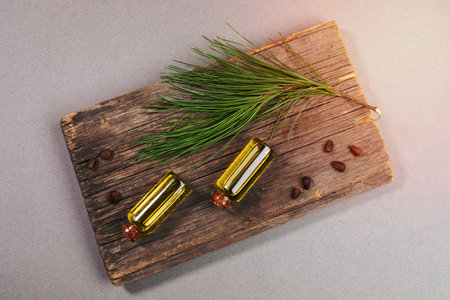 Top view two small glass bottles of essential cedar oil on old wooden board with cedar branch and nuts on grey background. Coniferous spa aromatherapy and spa products concept.の写真素材