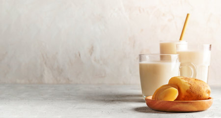 Vegan potato milk in different glasses and potato tuber and slices on wooden plate on neutral backdrop. Vegetable milk replacer. Healthy lactose free drink. Banner. Copy space. Selective focus.の写真素材