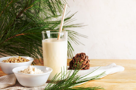 Cedar milk in glass and ingredients for it cooking flour and nuts, cone, branches on napkin on wooden table. Plant based non dairy alternative milk. Organic milk replacer. Healthy drink. Copy space.の写真素材