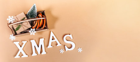 Top view to wooden box with Christmas decorations decorative Xmas tree, dry orange slices, DIY wrapped gift box, snowflakes and white letters XMAS on beige. Christmas banner. Horizontal orientation.の写真素材