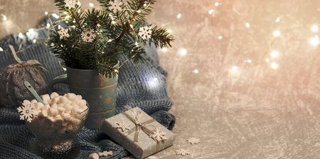 Xmas composition with fir twigs in mug, Xmas lights, DIY gift box, marshmallow, snowflakes on knitted grey plaid. Cozy warm homely winter Danish hygge concept. Selective focus. Copy space.の写真素材
