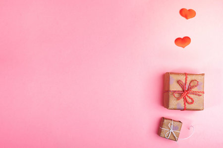 Two trendy diy wrapped gift boxes and two red hearts on pink background. Valentine's day, Women's day or Mother's day festive flat lay mockup. Zero Waste holiday. Top view, copy space.の写真素材