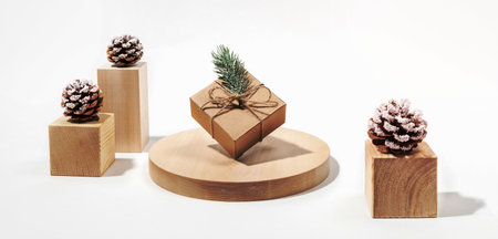 Xmas festive banner with cones and balanced DIY gift cardbox on wooden podiums on white background. Trendy modern minimalism and balance. Festive greeting card. Banner.の写真素材