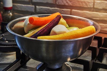 Carrots of three colors, in a metal bowl on gas stove.の写真素材