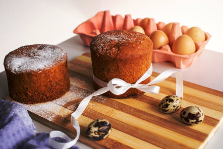Easter pastries , sponge cake with powdered sugar on a wooden board . Chicken and quail eggs. Place...