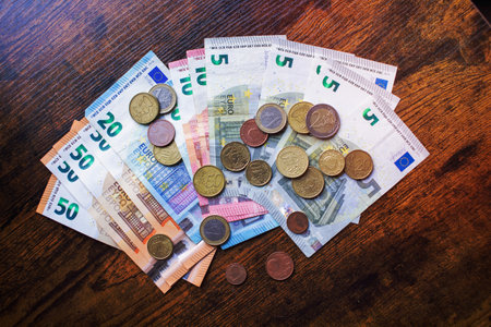 Euro banknotes of different denominations and coins lie on a wooden tableの写真素材