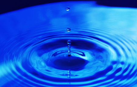 Drops falling in water and circles walking on water, with reflection. Blue background, texture.の写真素材