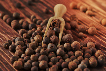 Large black peppercorns with wooden spatula are scattered over wooden vintage background.の写真素材