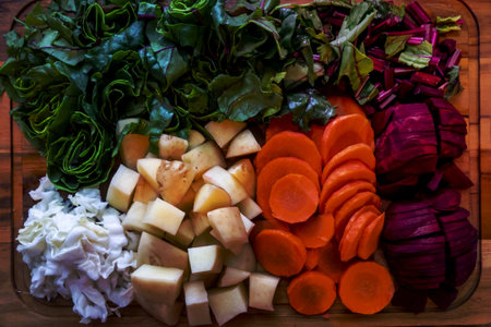 A board with ingredients for cooking delicious borscht on a wooden background. Cabbage, potatoes, carrots, beets with tops. Step-by-step process of slicing vegetables for beetroot soup High quality photoの写真素材