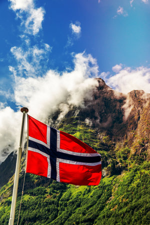 Norwegian national flag waving in the wind and mountain's peak in Neroy fjord,  Aurlan, Sogn og Fjordane county, Norwayの写真素材