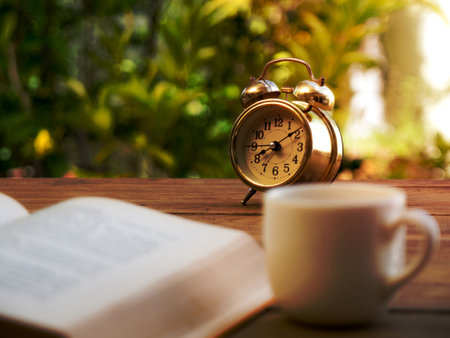 text book with vintage alarm clock and White coffee cup on the wood table. The background is green...