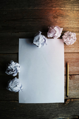 Crumpled up papers with a sheet of blank paper and a pencil on grey wooden backgroundの写真素材