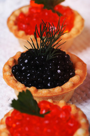 Three tartlets with red salmon caviar and sturgeon caviar black closeup. verticalの写真素材