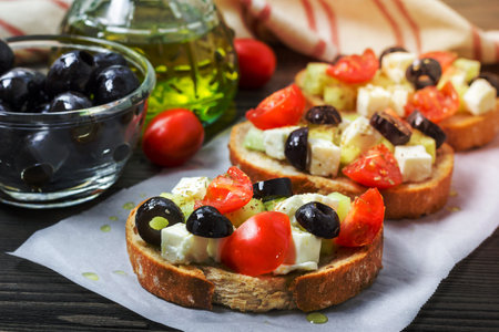 Greek style crostini with feta cheese, tomatoes, cucumber, olives and herbsの写真素材