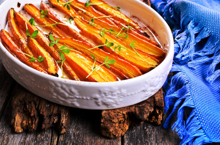 Baked carrots in a baking dish with vegetable oil on a wooden surfaceの写真素材
