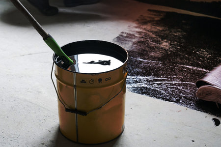 Applying hot resin to the floor for waterproofing, roller and bucket of resin, black and liquid...
