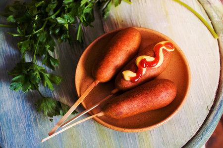 corndog sausage on a stick with mustard, ketchup and parsleyの写真素材