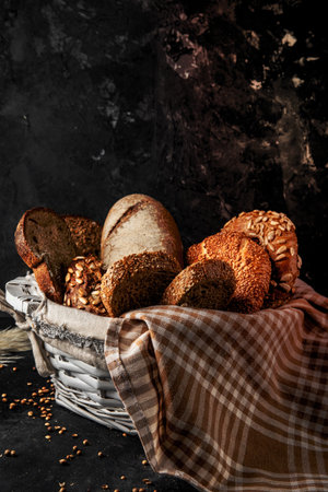side view of basket full of breads as bagel baguette rye on black surface and black background